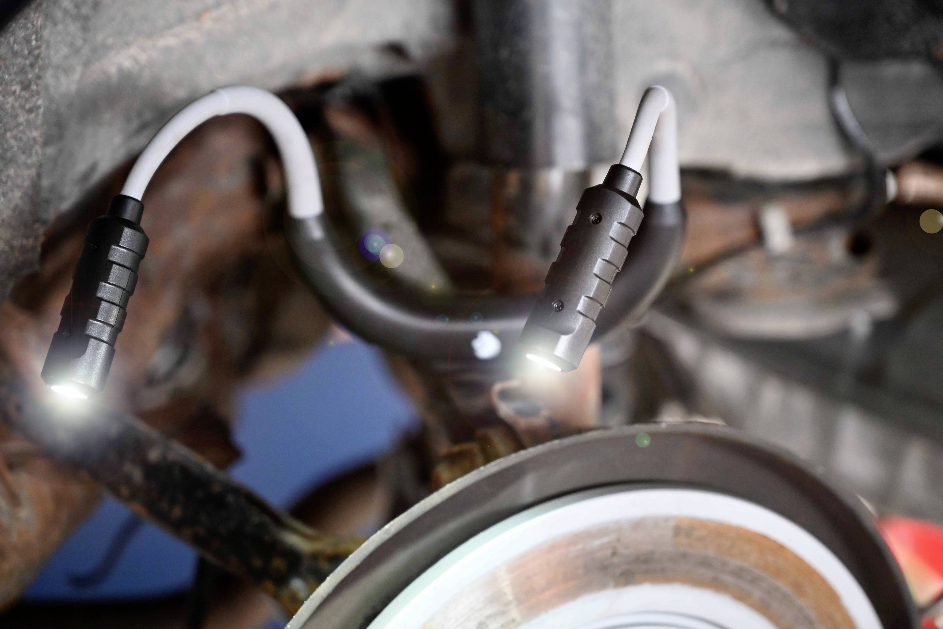 Two flexible LED lamps illuminate an area underneath a vehicle, potentially for inspection or repair.