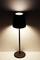 A switched-on table lamp with a black shade, casting soft light onto a white surface, is the focal point of the image.