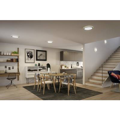 A modern dining room with a table and chairs, a staircase to the right and a kitchen in the background. Subtle lighting and wall decoration.