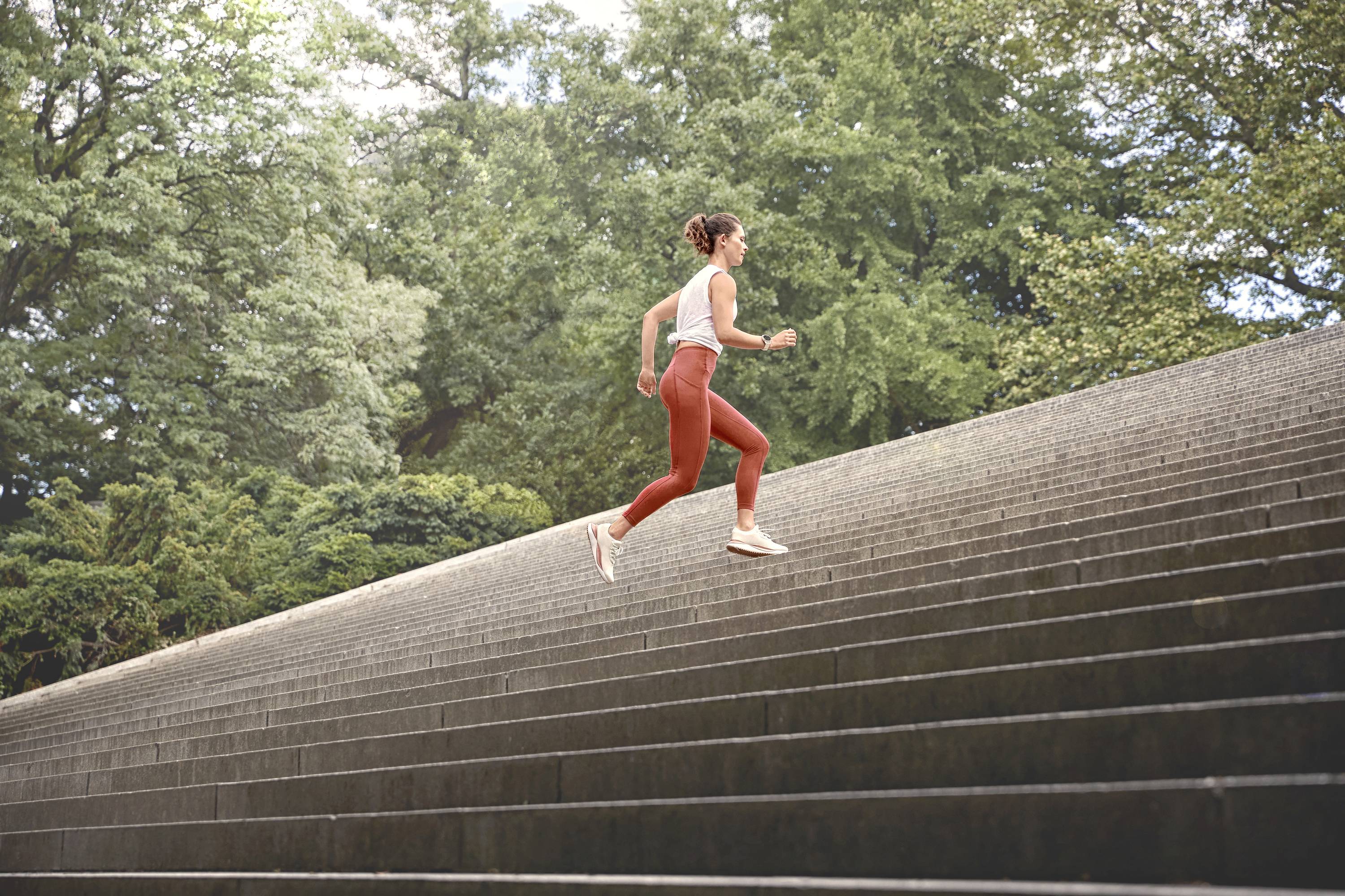 A woman in sportswear is running up a long outdoor staircase, surrounded by lush greenery and trees.