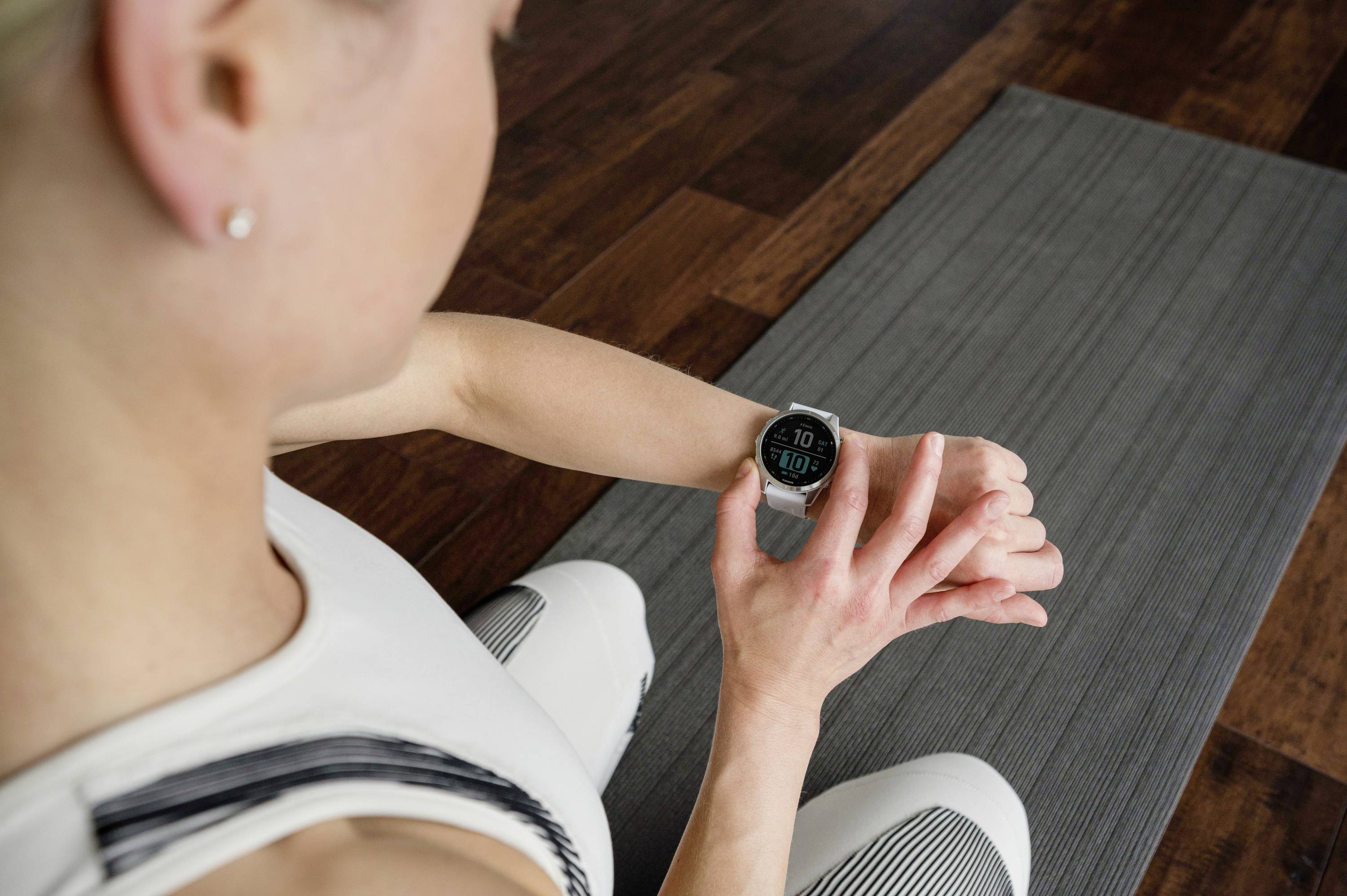 Woman in sportswear checking smartwatch while training on yoga mat. The watch displays steps and time, with a wooden environment.