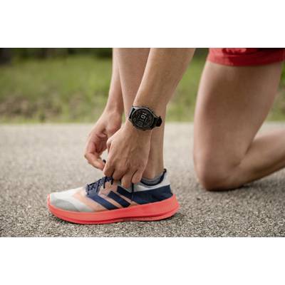 A person is kneeling on a path and tying the laces of a trainer. The person is wearing a watch and is dressed in sportswear.