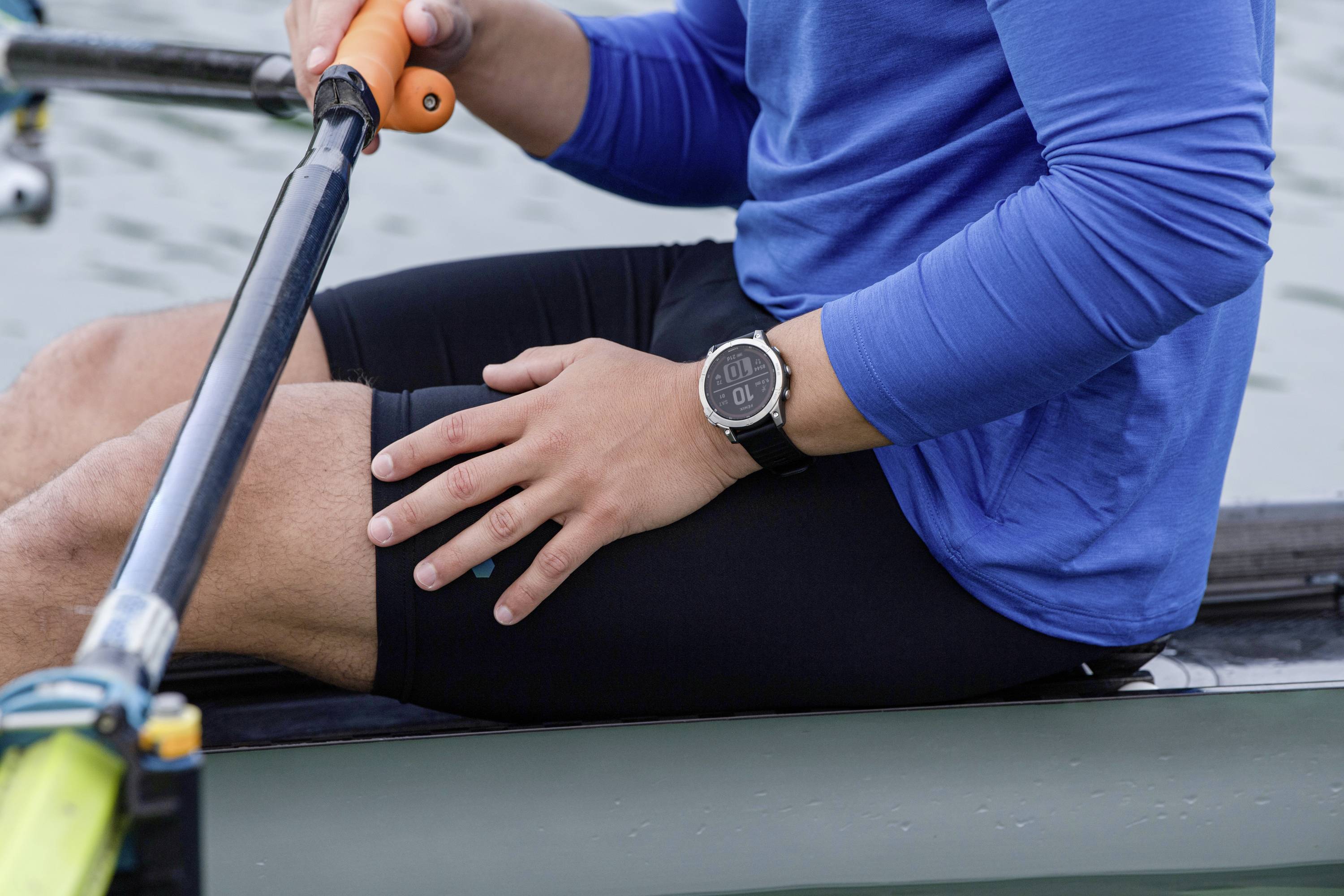 A person in a blue shirt is sitting in a rowing boat and holding an oar. They are wearing a wristwatch.