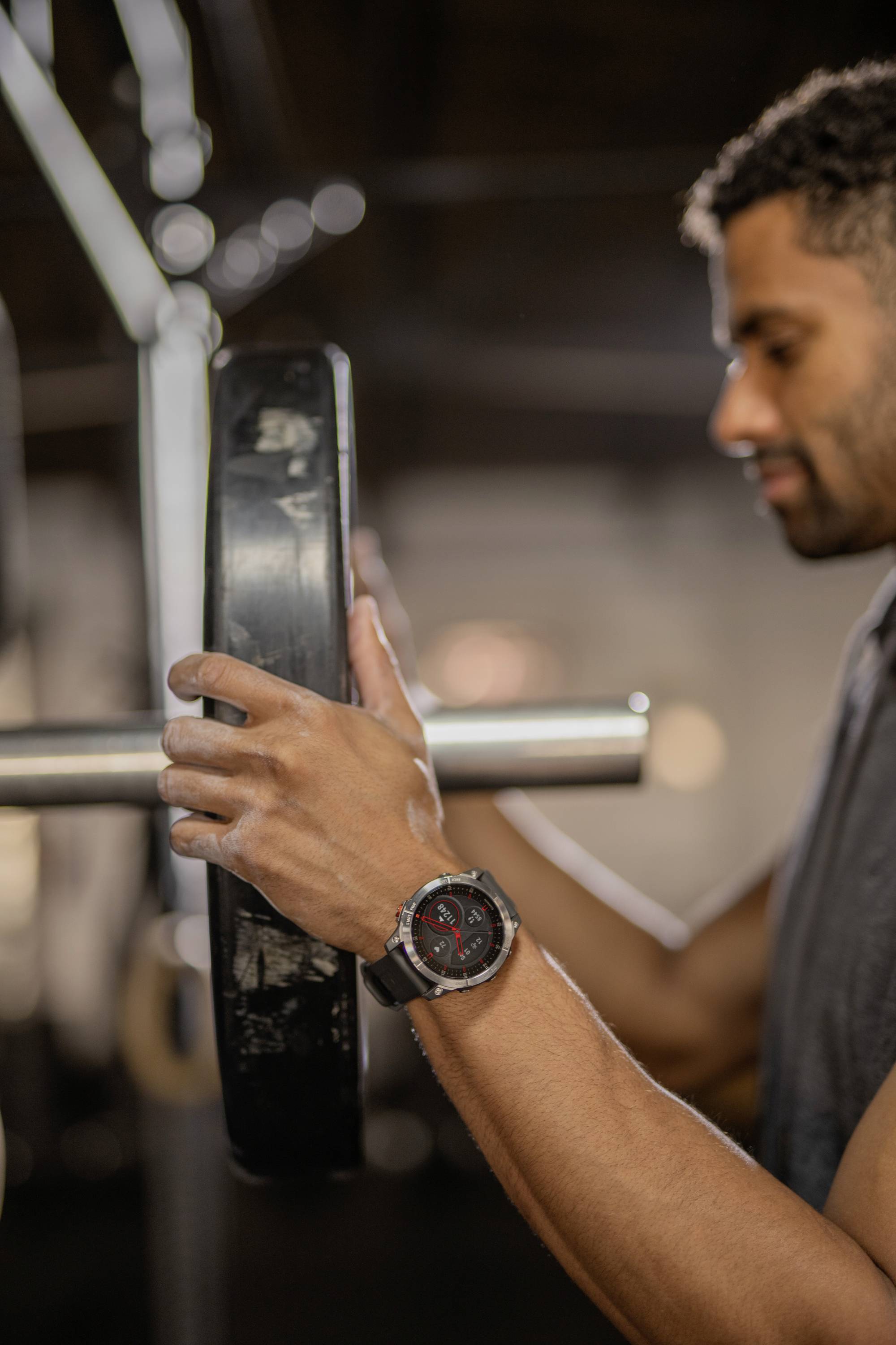 A person in the gym is placing a weight on a barbell. The focus is on the hands and the weight.