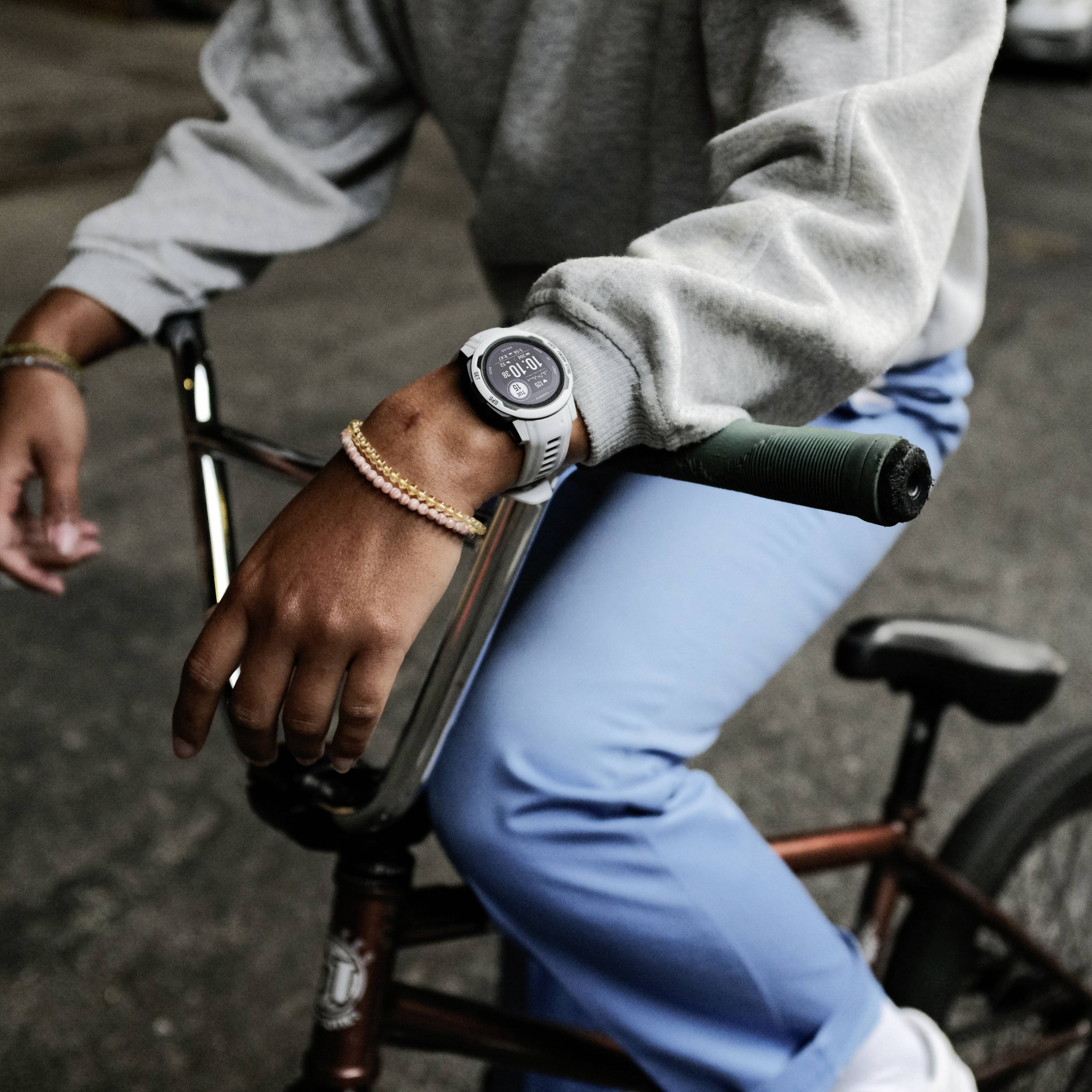 A person is cycling, with a close-up of their hands on the handlebars. They are wearing blue trousers, a grey jumper, a bracelet and a watch.