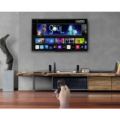 A living room with modern furnishings. A television mounted on the wall displays a streaming service menu. Someone is holding a remote control.