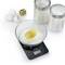 A kitchen scales shows 128g of flour with an egg on top. Beside it are three eggs, a piece of butter, and two containers with ingredients.
