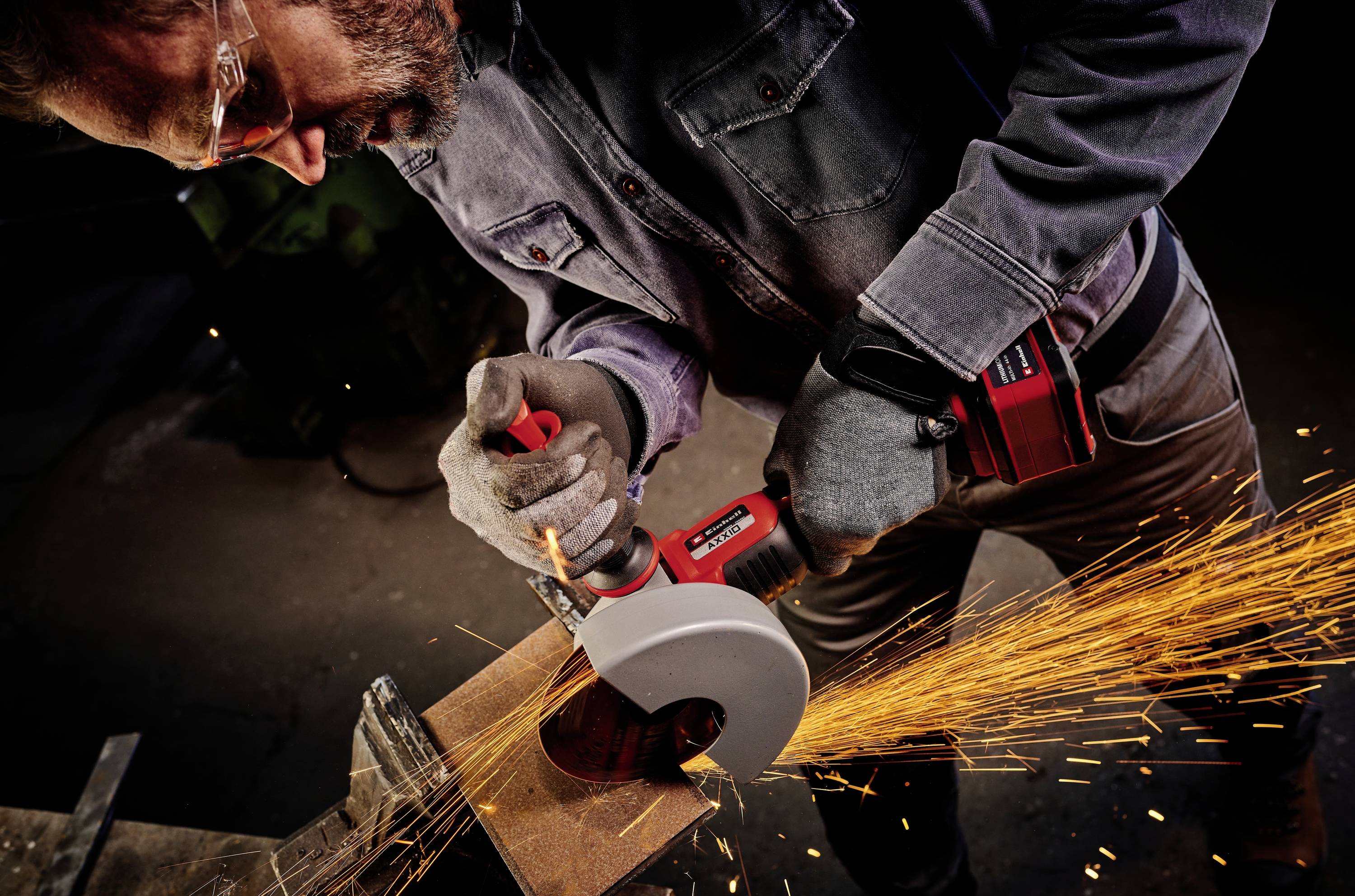 'A man is wearing safety glasses and using an angle grinder, with sparks flying as he cuts metal. He is wearing protective clothing.'