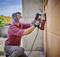 A man is wearing safety glasses and a respiratory mask while working with an electric tool on a concrete wall.