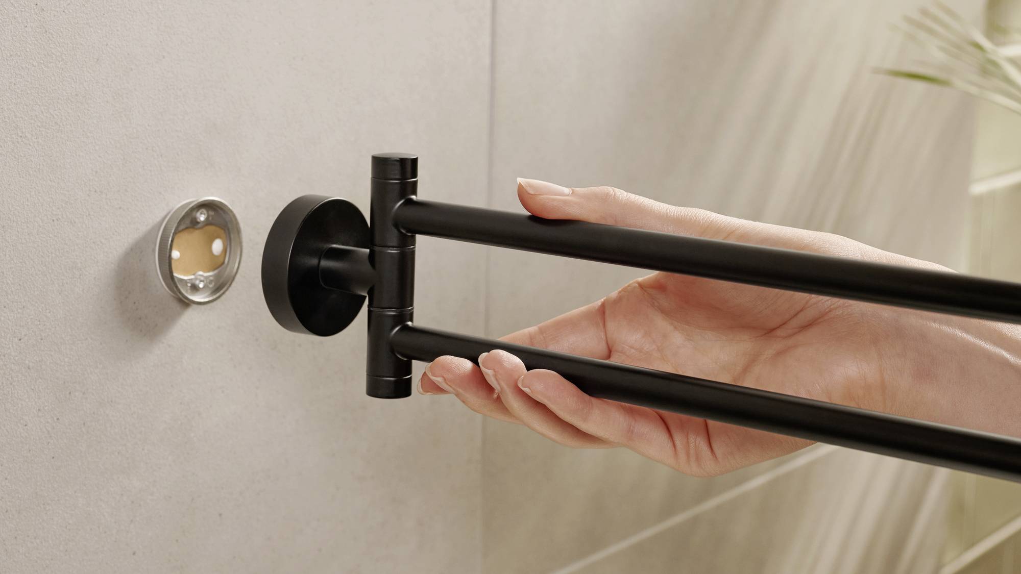 A hand is mounting a black towel rail on a bathroom wall. The fitting is designed in a simple and modern style.