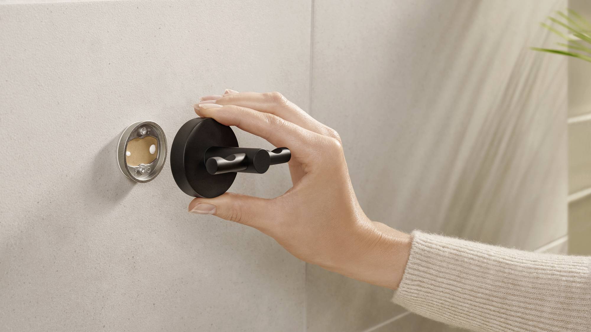 'A hand is installing or removing a round, black door handle from a wall.'