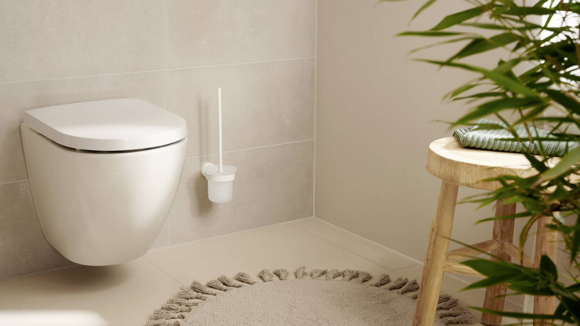 Modern bathroom view with wall-mounted toilet, round rug, plants and wooden chair. Bright and cosy atmosphere.
