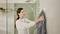 A woman is hanging a grey towel in a modern bathroom, in front of light green tiles and a rainfall shower.