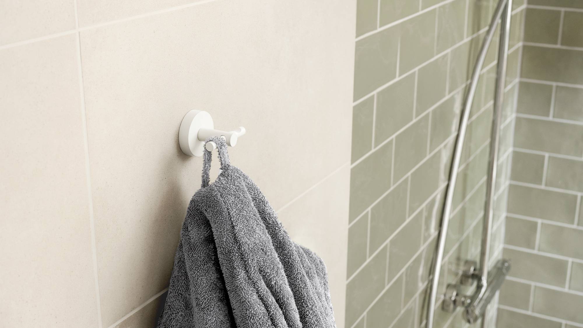 A grey towel hangs on a hook beside a shower cubicle with beige tiles.