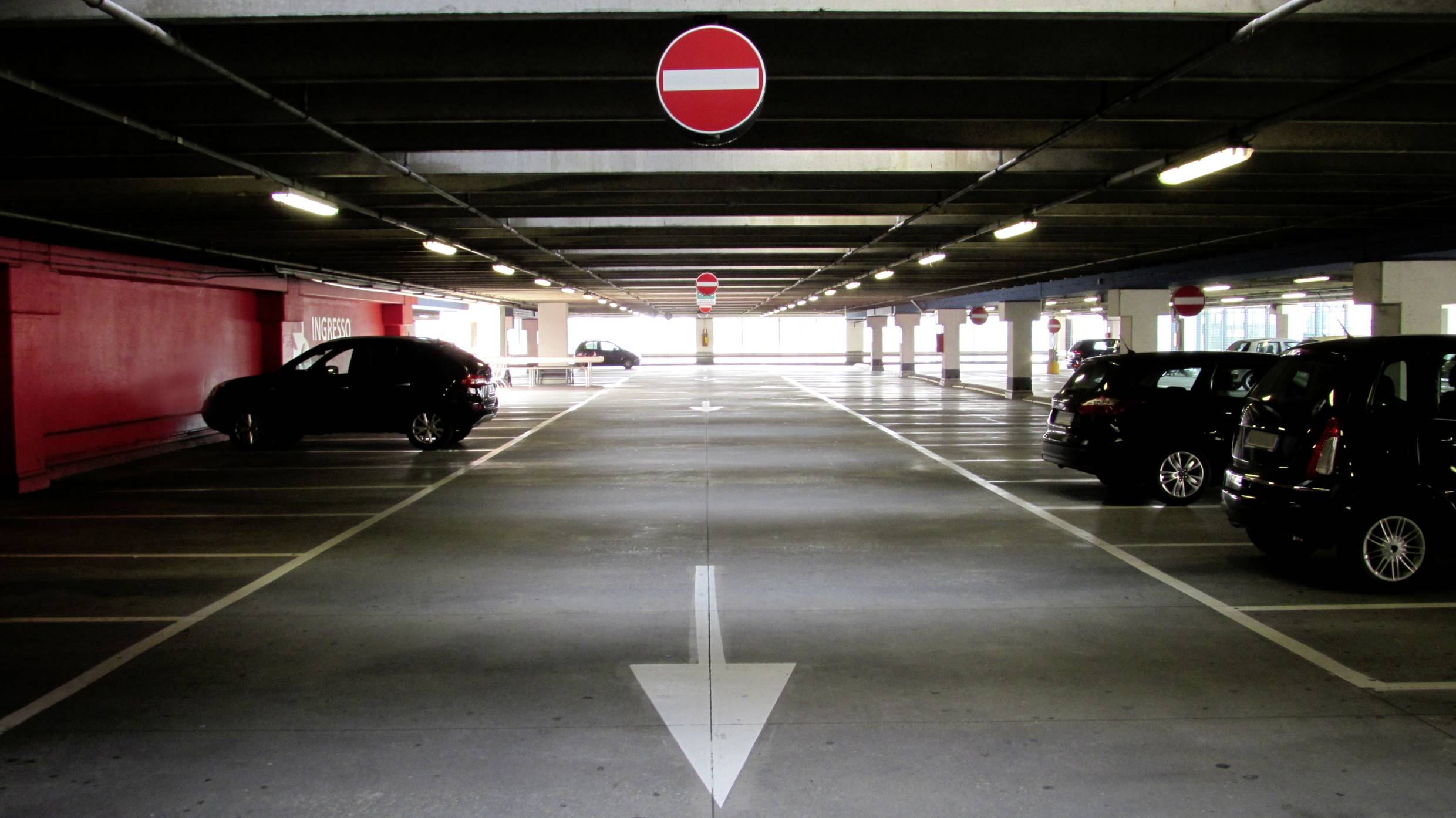 A nearly empty multi-storey car park with a large white arrow on the ground. Red 'No Entry' signs are visible.