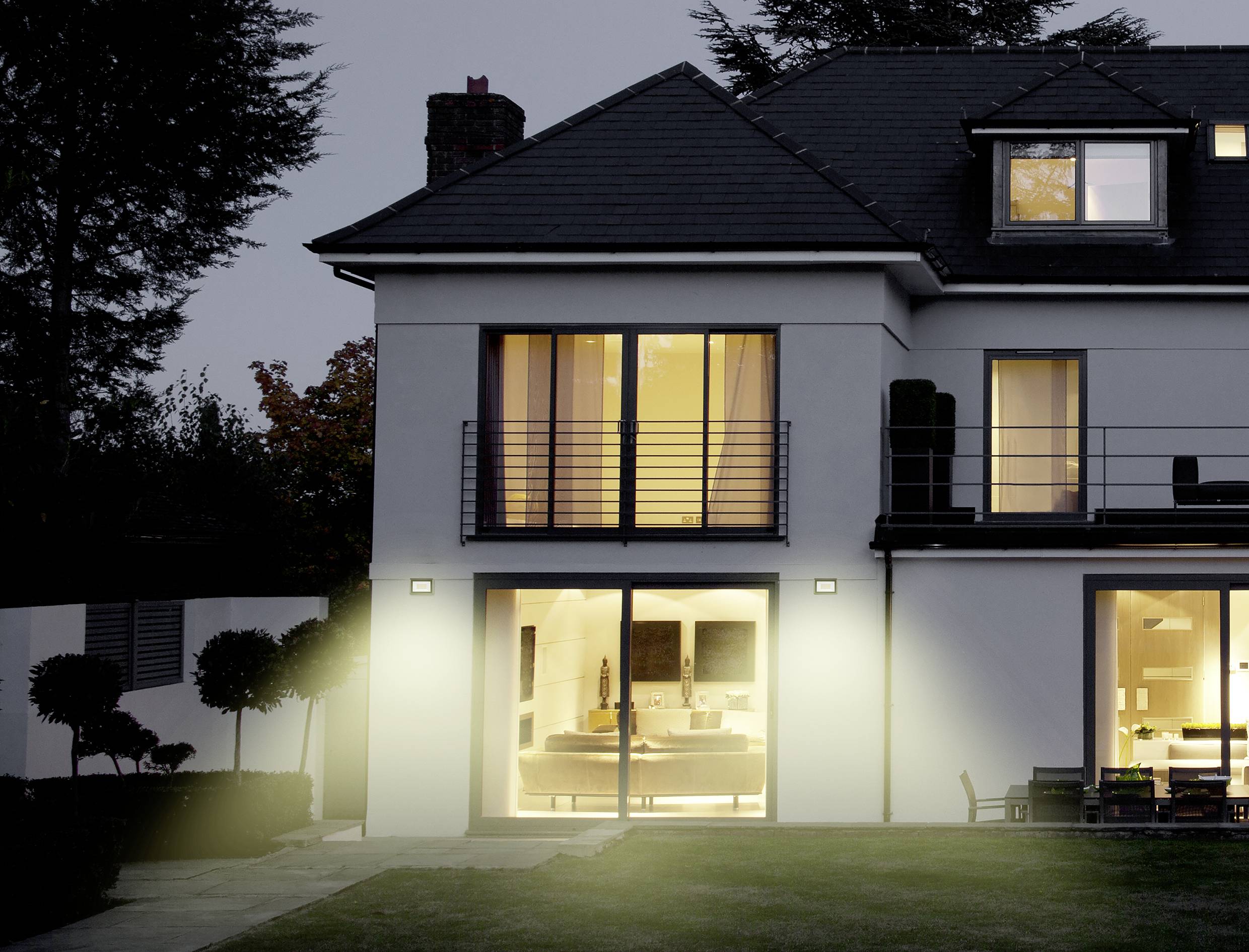 Two-storey modern house at dusk, with illuminated interior and well-maintained garden.