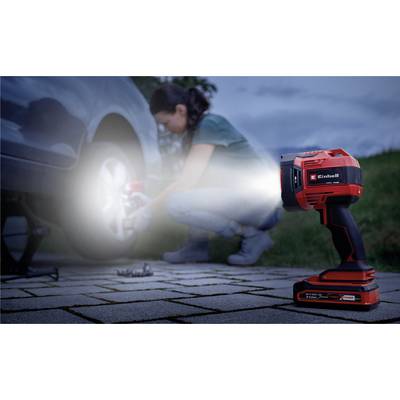 A person is changing a car tyre in the evening with the help of a torch illuminating the wheel. Light grass can be seen in the background.