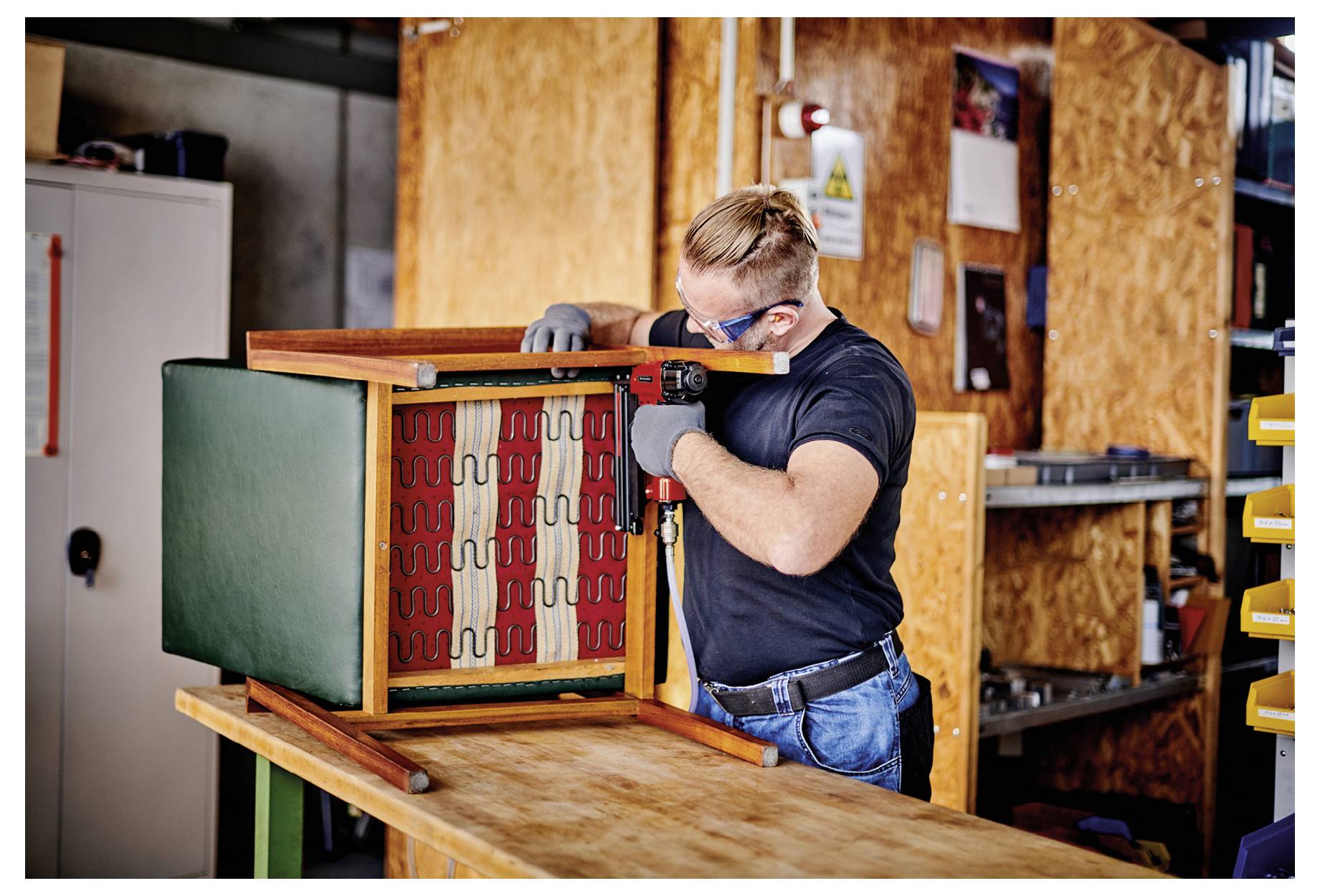 A man wearing safety glasses and gloves adjusts a large machine or cabinet in a workshop.