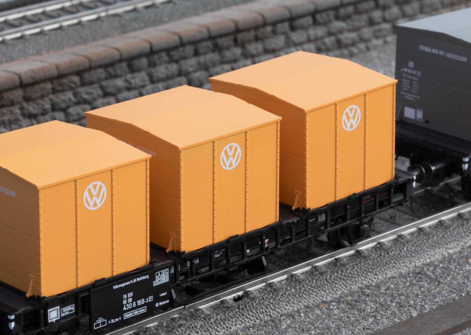 Three yellow freight containers with Volkswagen logo on a goods train. Background shows railway tracks and a stone wall.