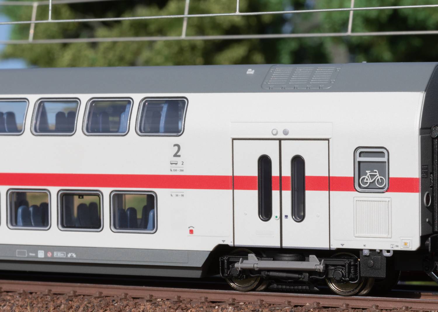 Double-decker train with bicycle symbol, suitable for passengers with bicycles, travelling on a track through green countryside in the background.