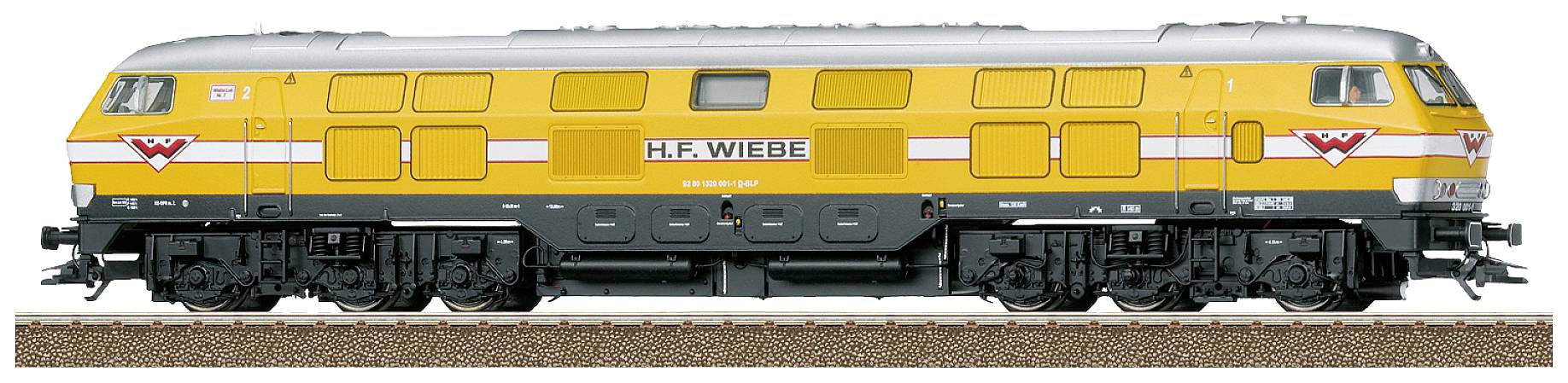 A yellow locomotive from the H.F. Wiebe brand is standing on a railway track. The locomotive is two-coloured in yellow and grey, with red accents.