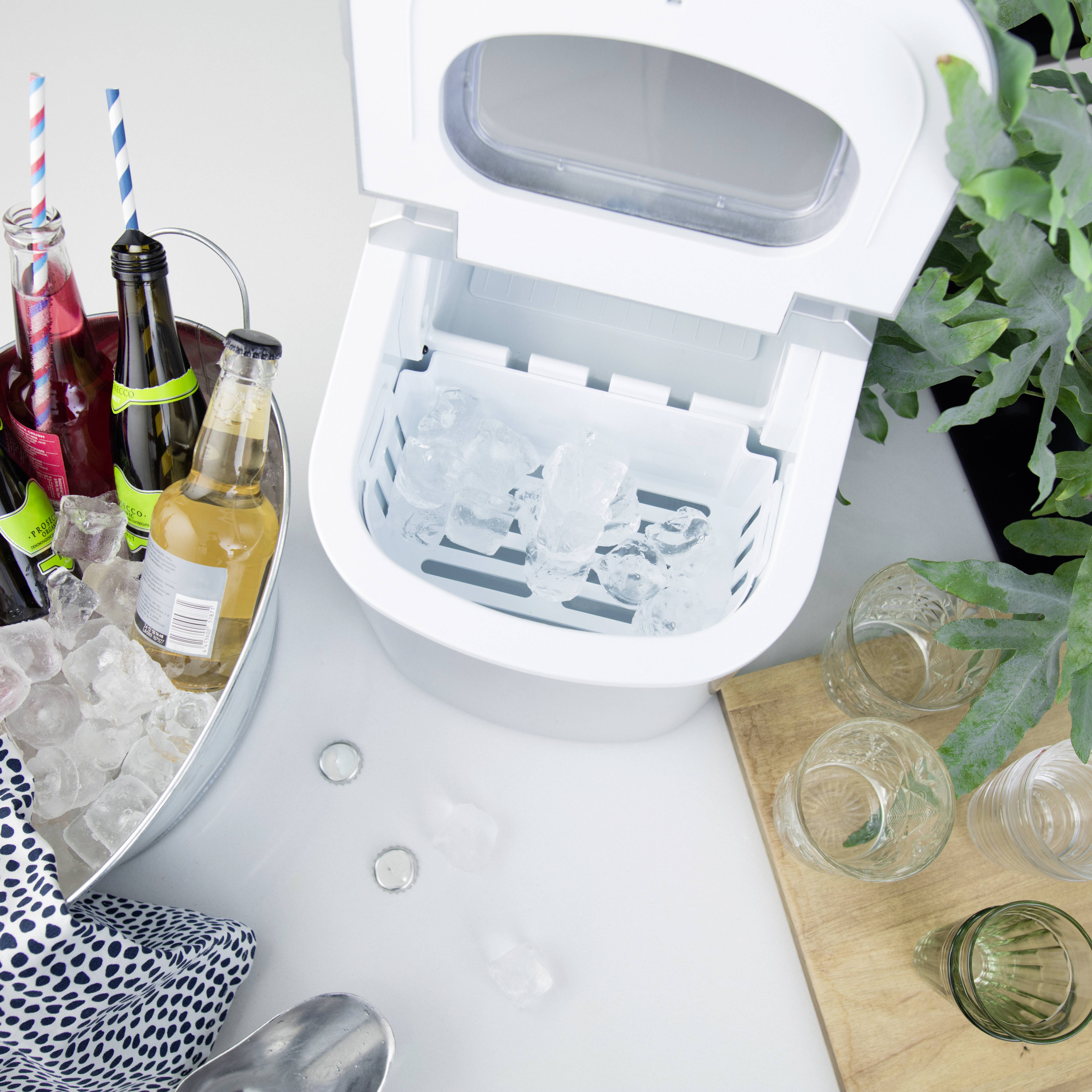 An ice machine with an open lid and ice cubes. Beside it, drinks in bottles and a bucket of ice, surrounded by a wooden board with glasses.