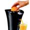 A hand is pressing an orange onto a black juicer. Fresh orange juice is flowing into a glass below.