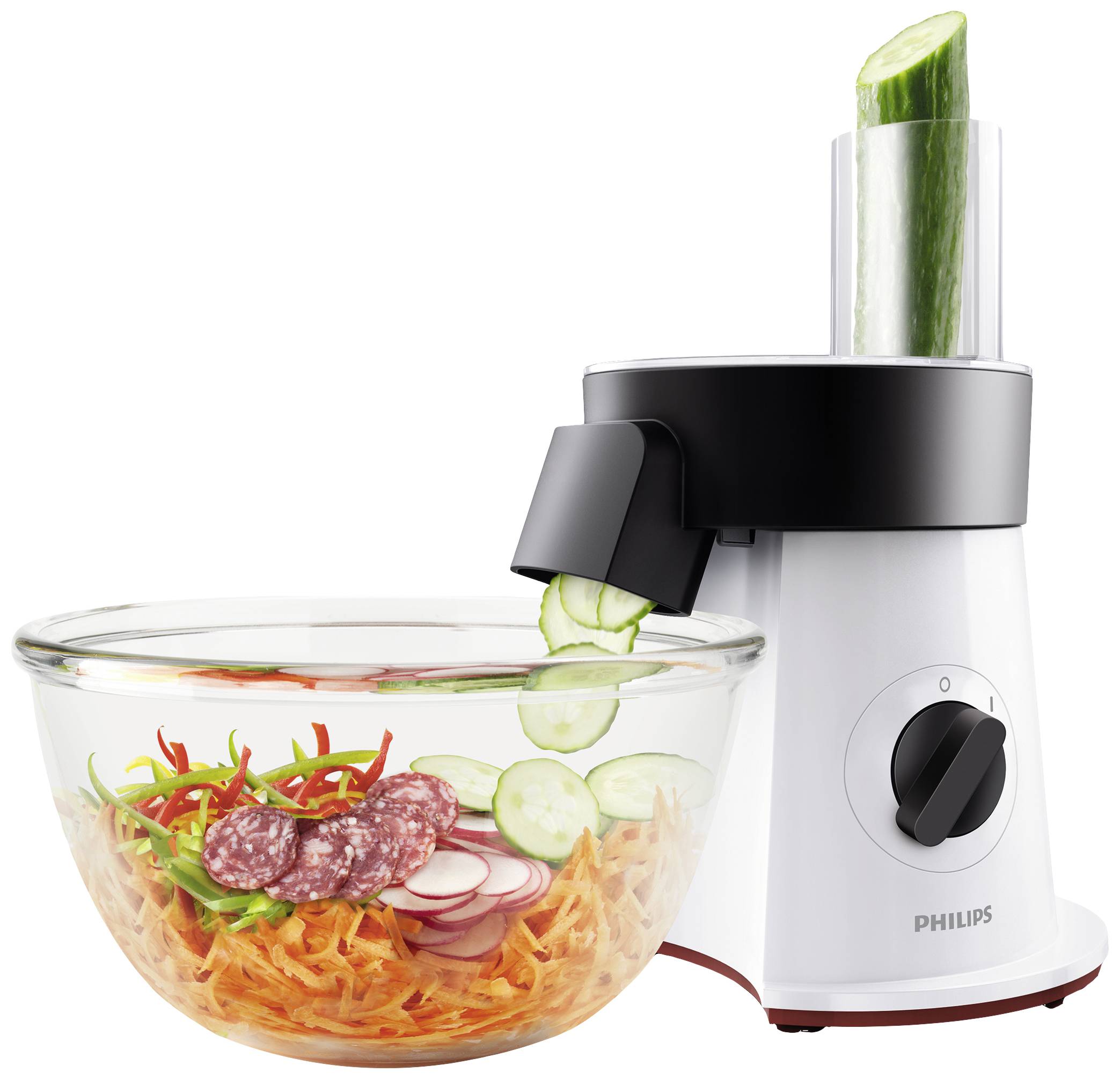 Kitchen food processor with cucumber attachment slices cucumber into a glass bowl with carrots, radishes, and salami.