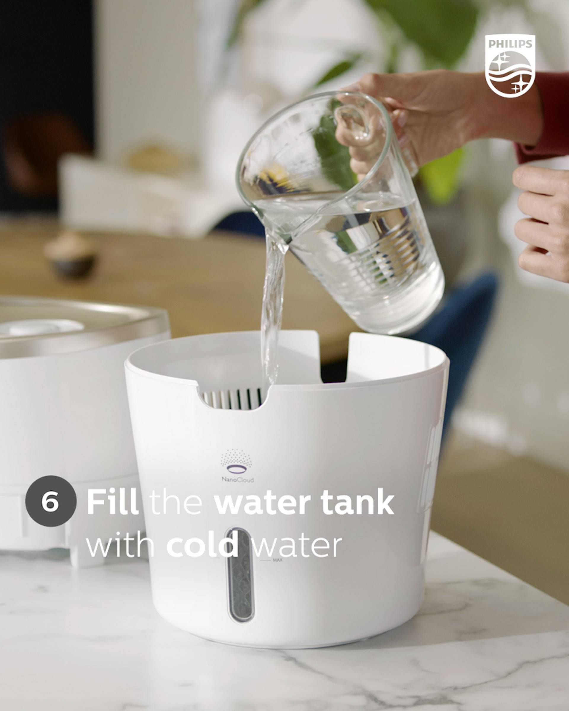 'Fill the water tank with cold water.' A glass is being poured into a white water tank on a kitchen worktop.