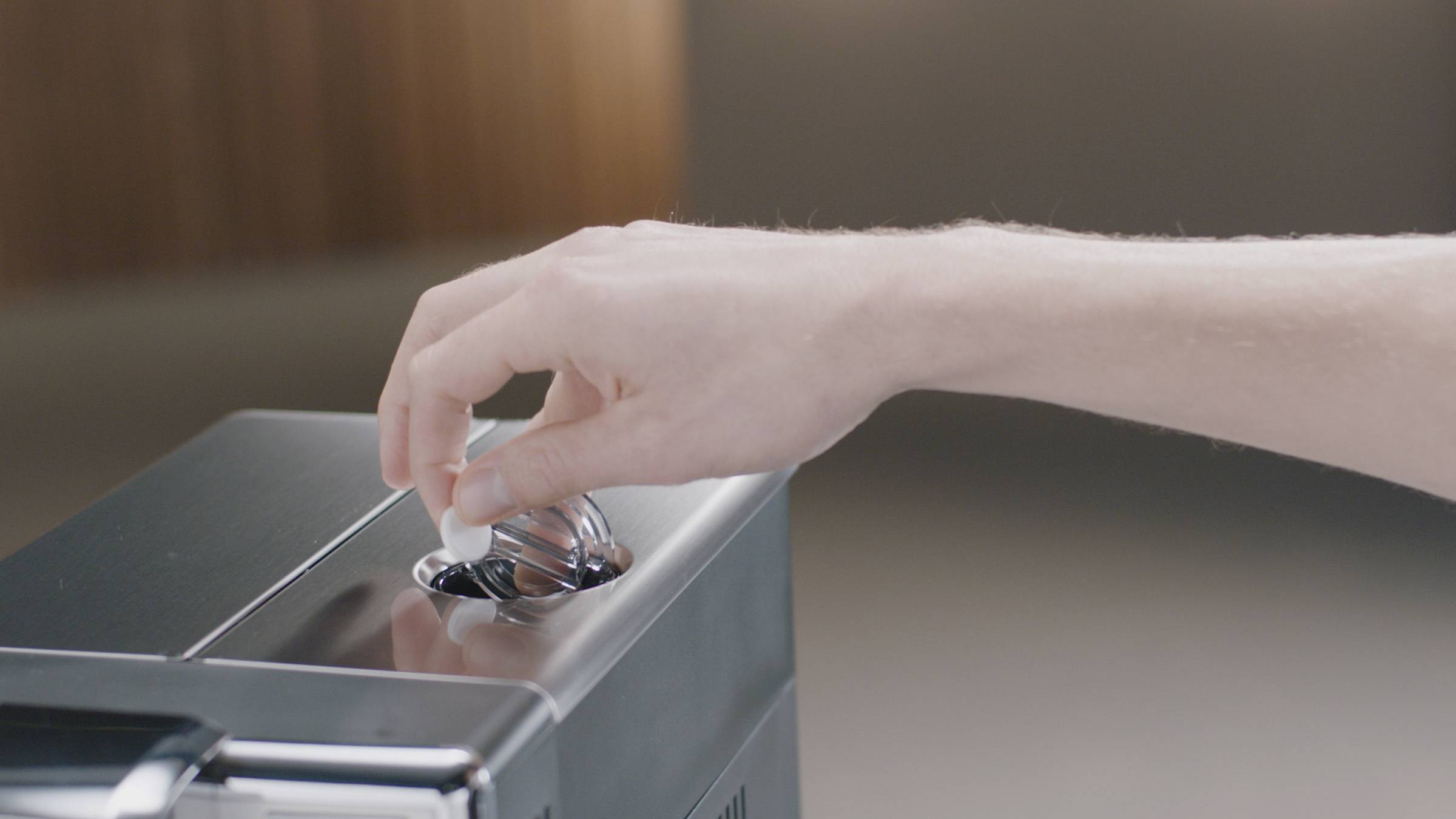 A hand is inserting a coffee capsule into a coffee machine.