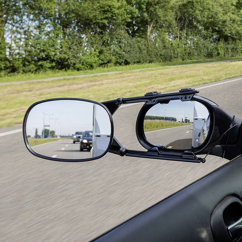 A car drives on the motorway, with the reflection showing other vehicles behind the car. A clear sky and green landscape surround the road.