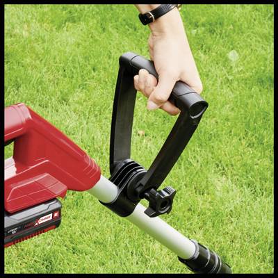 A person is holding a red cordless lawn trimmer over green grass. Their hand grips the device's handle, ready to trim.