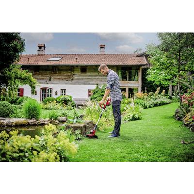 A man tends the lawn in the garden of a traditional country cottage. The surroundings are green and blooming.