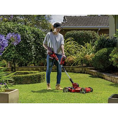 A person is mowing a lawn with an electric lawnmower in a well-maintained garden.