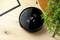 A round, black robot vacuum cleaner with a touch control panel on a wooden floor next to a table and a green plant.