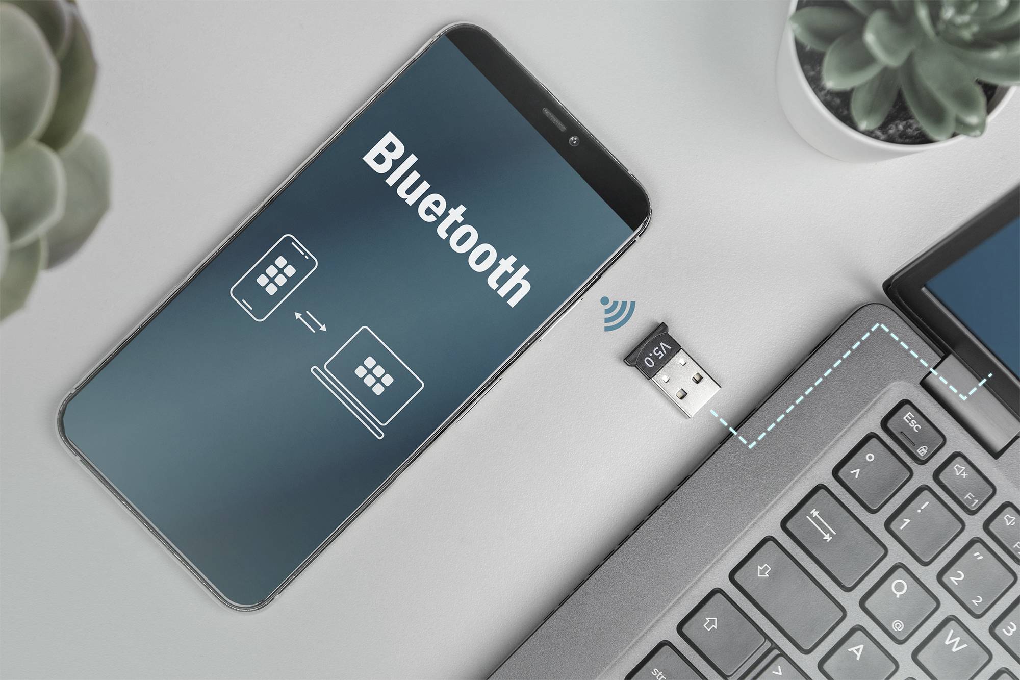 A smartphone shows a Bluetooth connection to a laptop. A Bluetooth USB dongle is plugged into the laptop.
