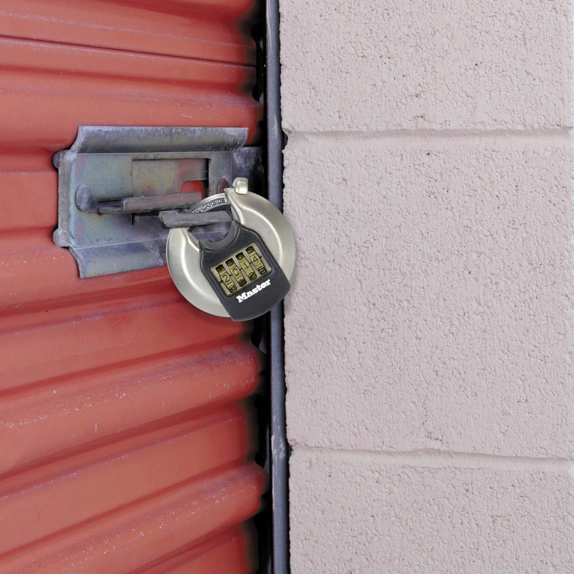 A red garage door is secured with a combination lock. The lock is hanging on a metal bar that is mounted on the wall.