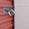 A red garage door is secured with a combination lock. The lock is hanging on a metal bar that is mounted on the wall.