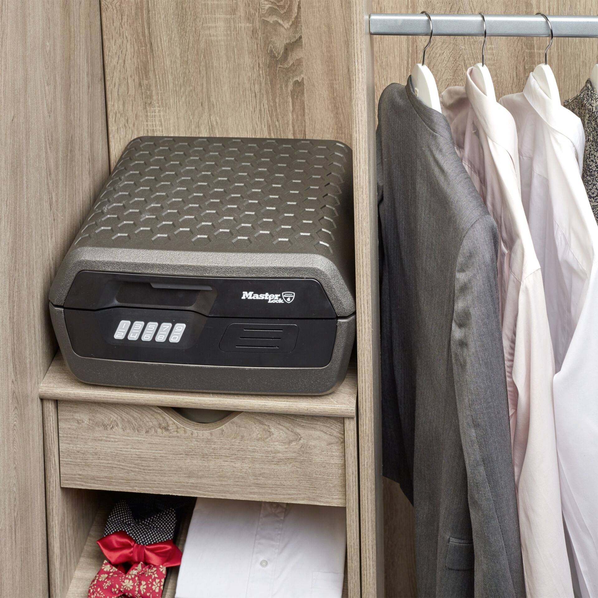 An open wardrobe door reveals a safe on a shelf, with shirts hanging on a clothes hanger. Beneath them lies a red bow tie.
