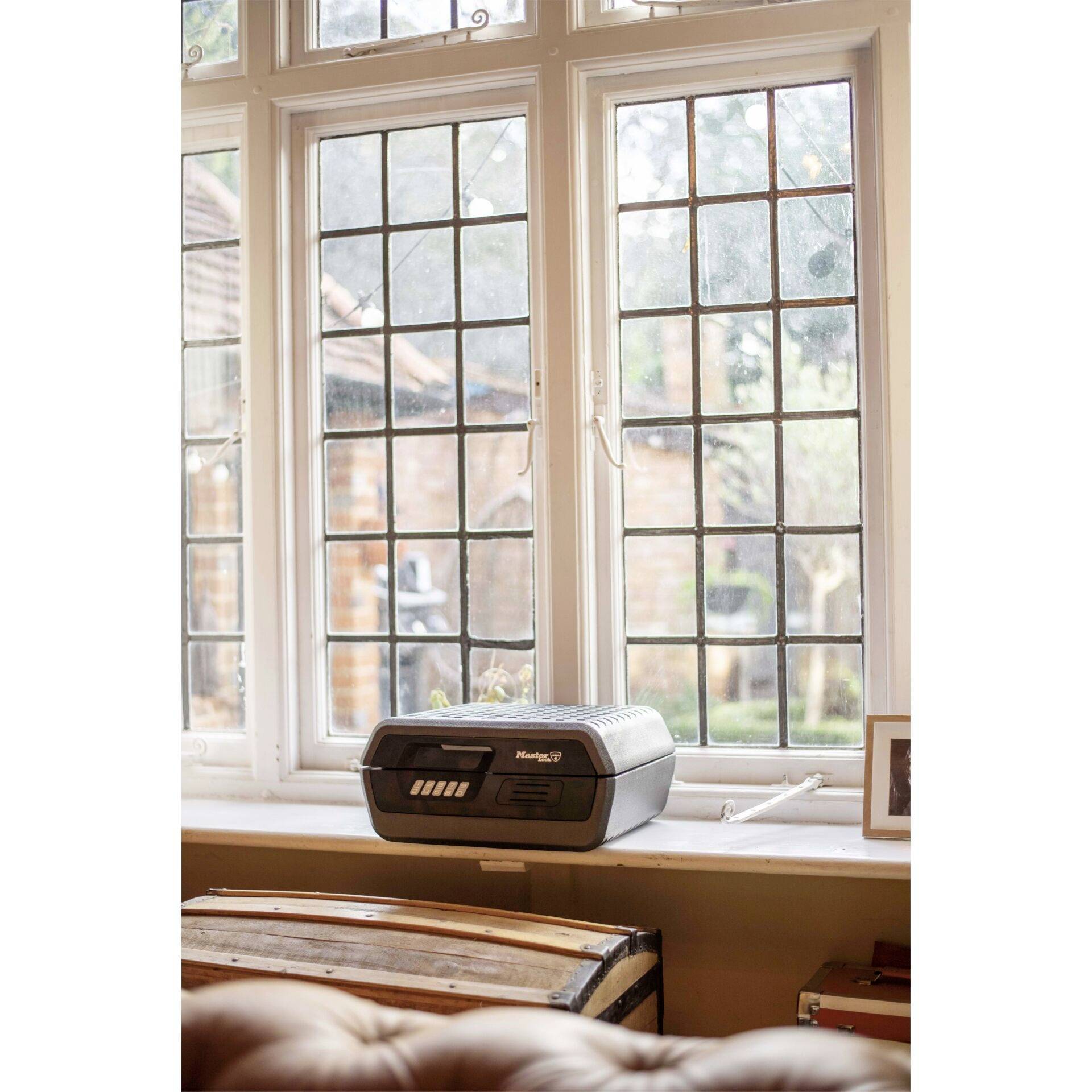 An antique radio sits on a windowsill, with a mullioned window in the background revealing a view of a garden.
