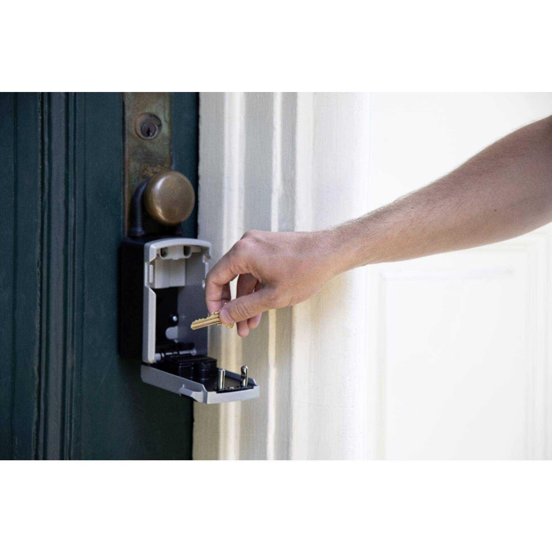 A hand is placing a bunch of keys into an open key safe mounted on a door. The safe is attached to the wall.