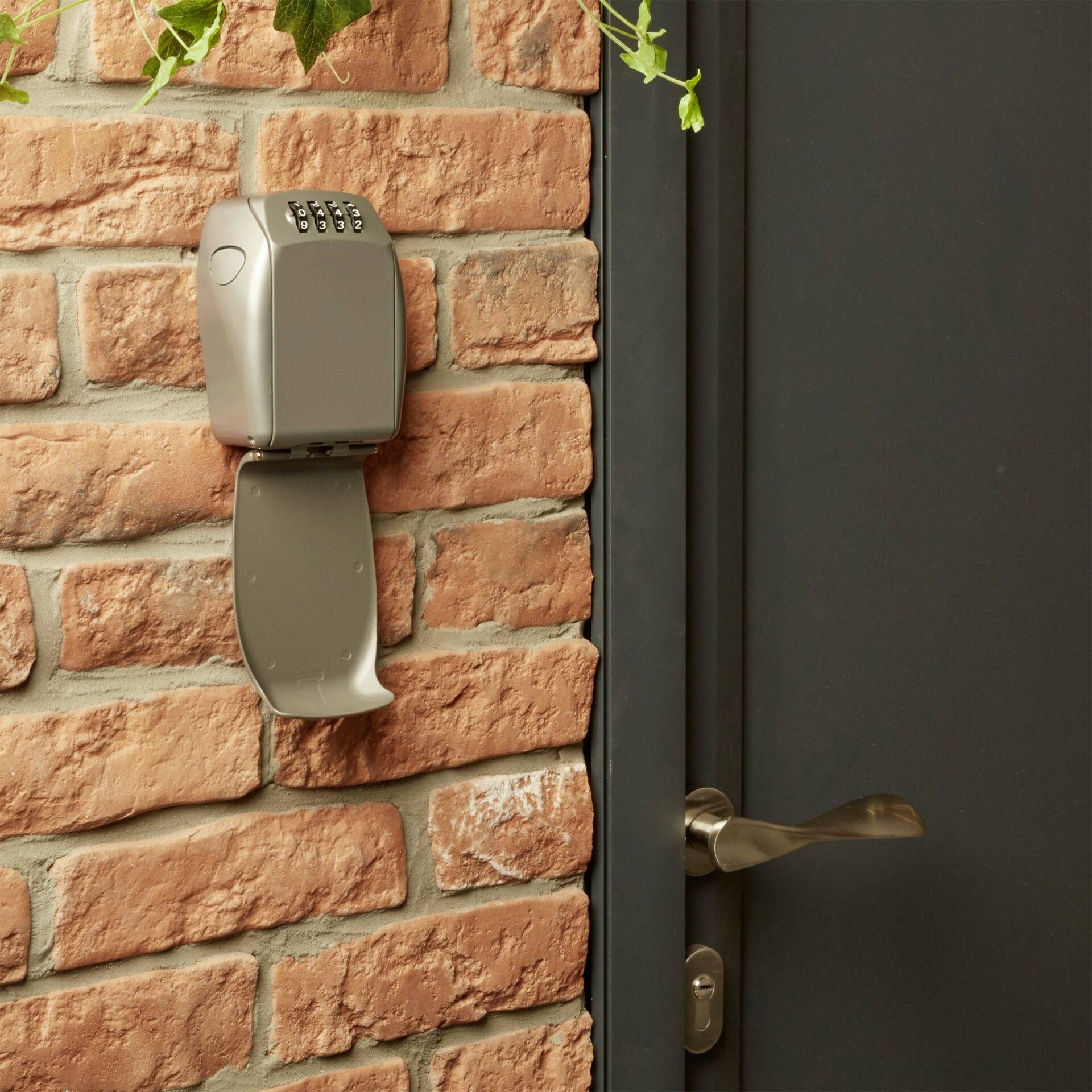 Key safe on a brick wall next to a closed door. The safe has a numeric lock for securely storing keys.<br><br>Note: The translation is already in British English, so no further changes were needed.