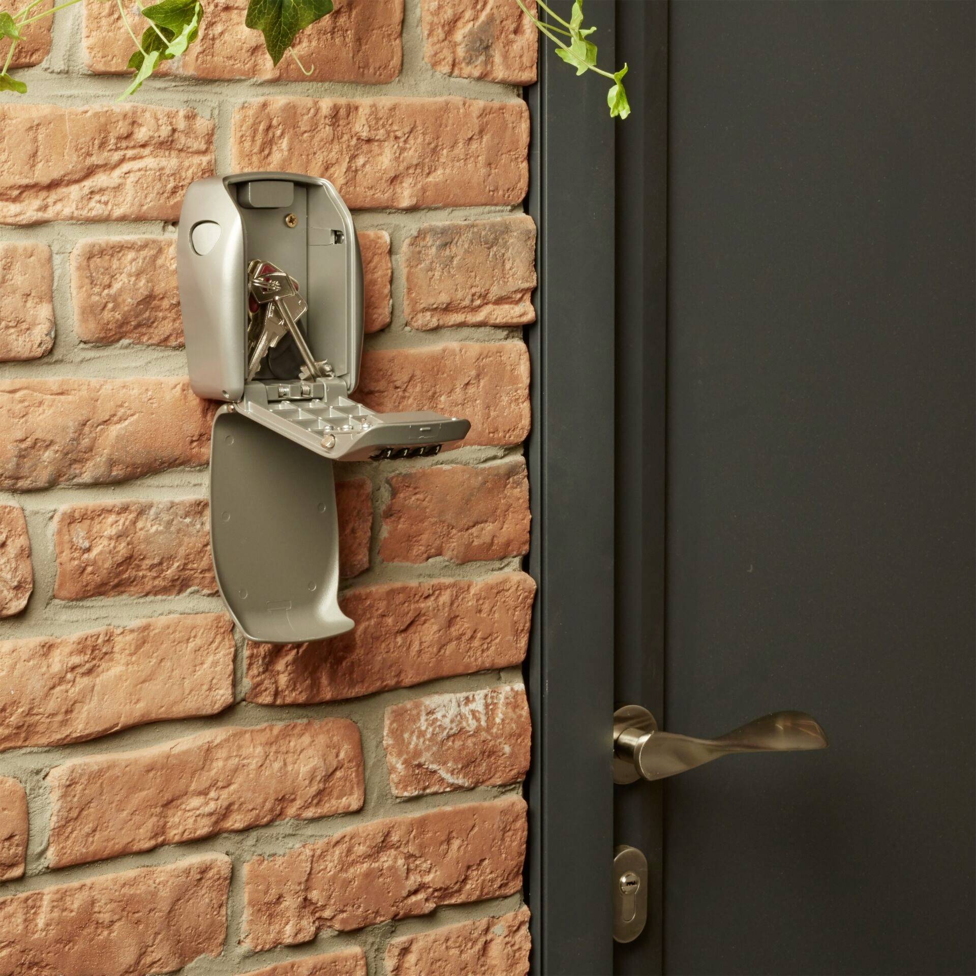 An open key cabinet mounted on a brick wall, next to a door. A bunch of keys is inside the cabinet.