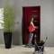 A woman with a red bag opens a red door, with a pushchair beside her. Next to it stands a large plant in a black pot.