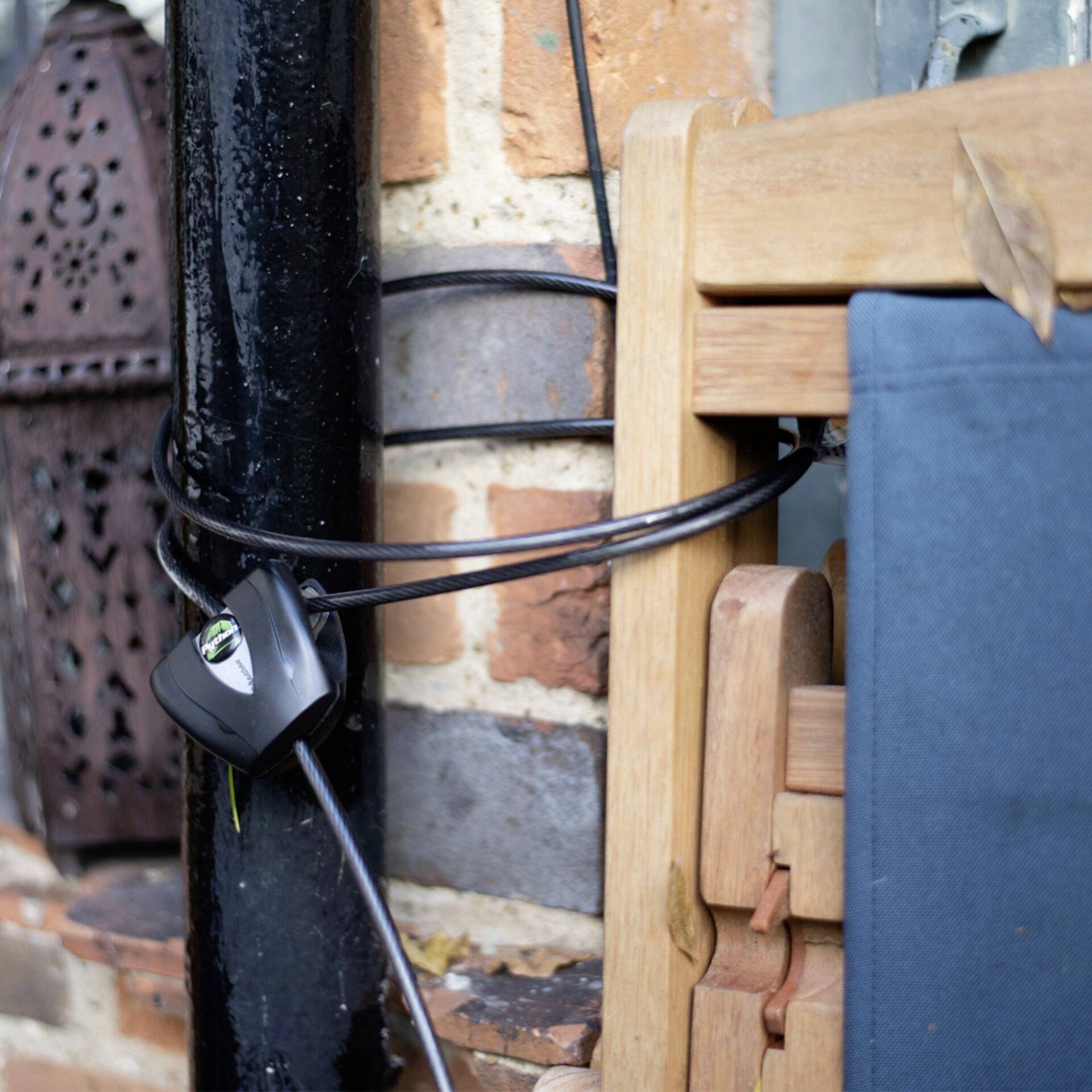 A bundle of black cables is wrapped around a metal pipe fixed to a brick wall. Next to it are stacked wooden chairs.