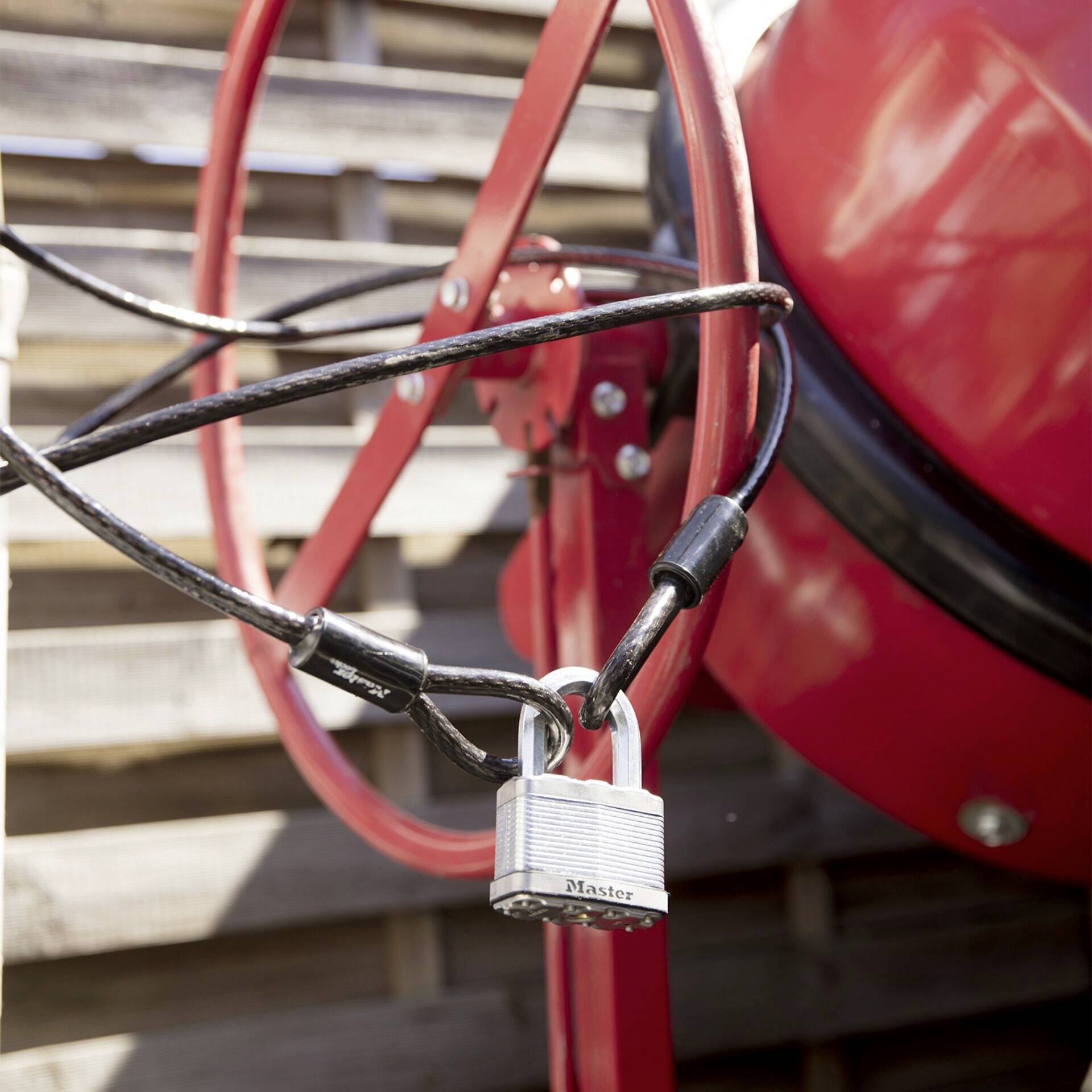 A mixer with a red frame is secured by a padlock. A wooden lattice fence is visible in the background.