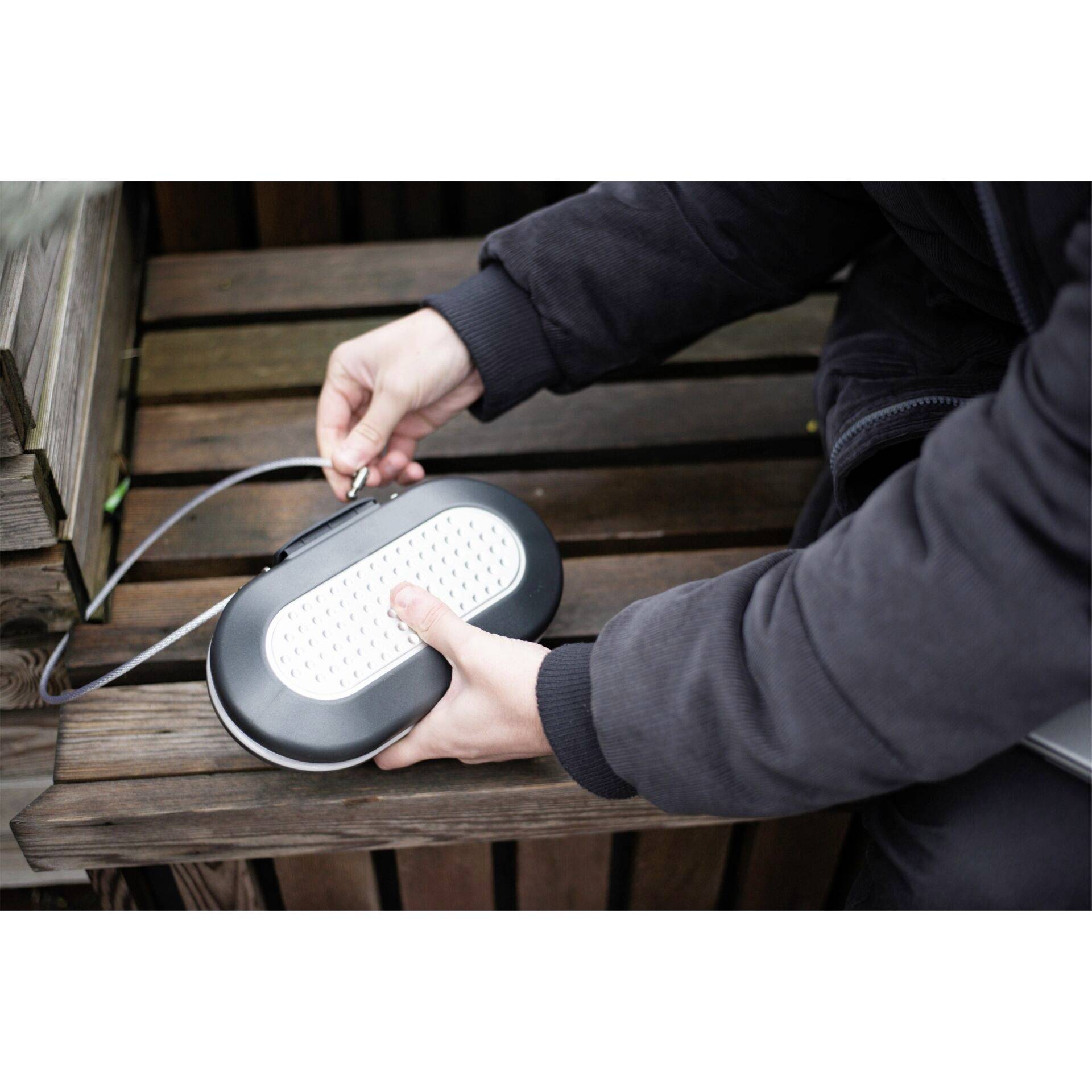 A person securing a padlock with a cable locking system on a wooden table, possibly for theft prevention.