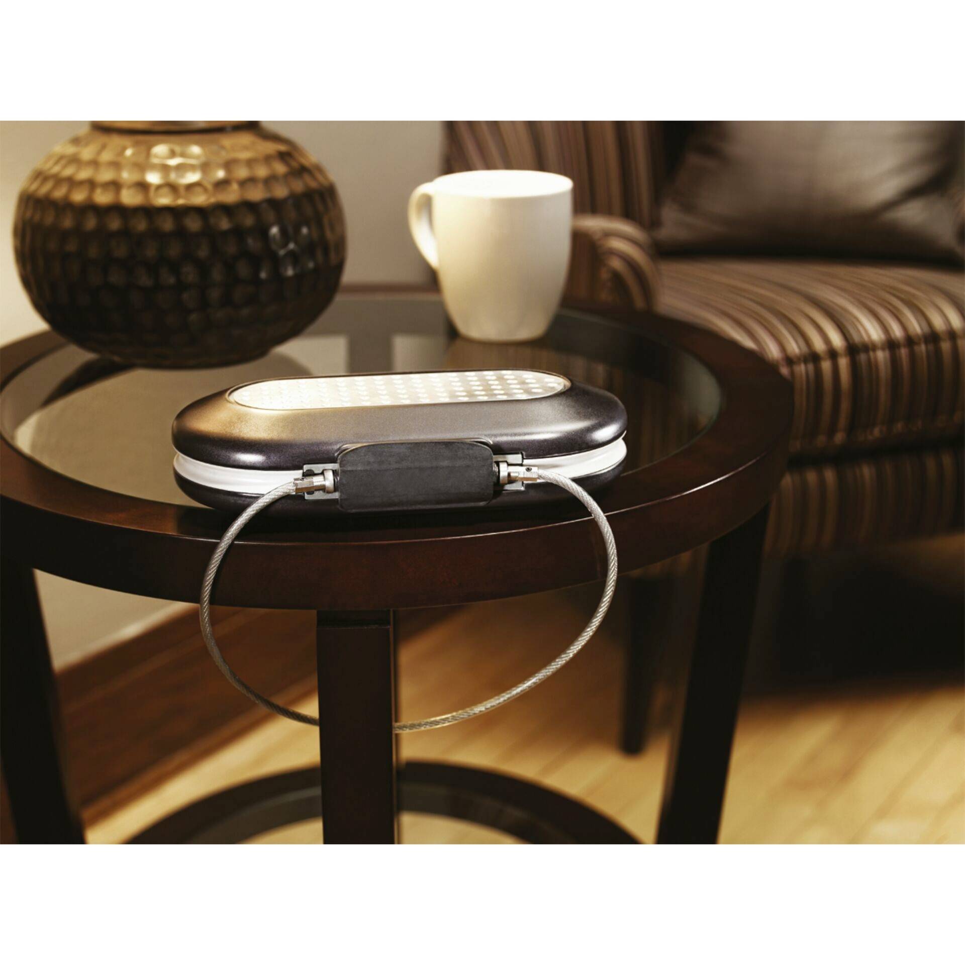 A small, locked storage container on a round wooden table, next to a cup, in front of a striped upholstered armchair.