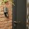 Wall safe with a combination lock next to a door on a brick wall, slightly ajar, with hanging green plants.
