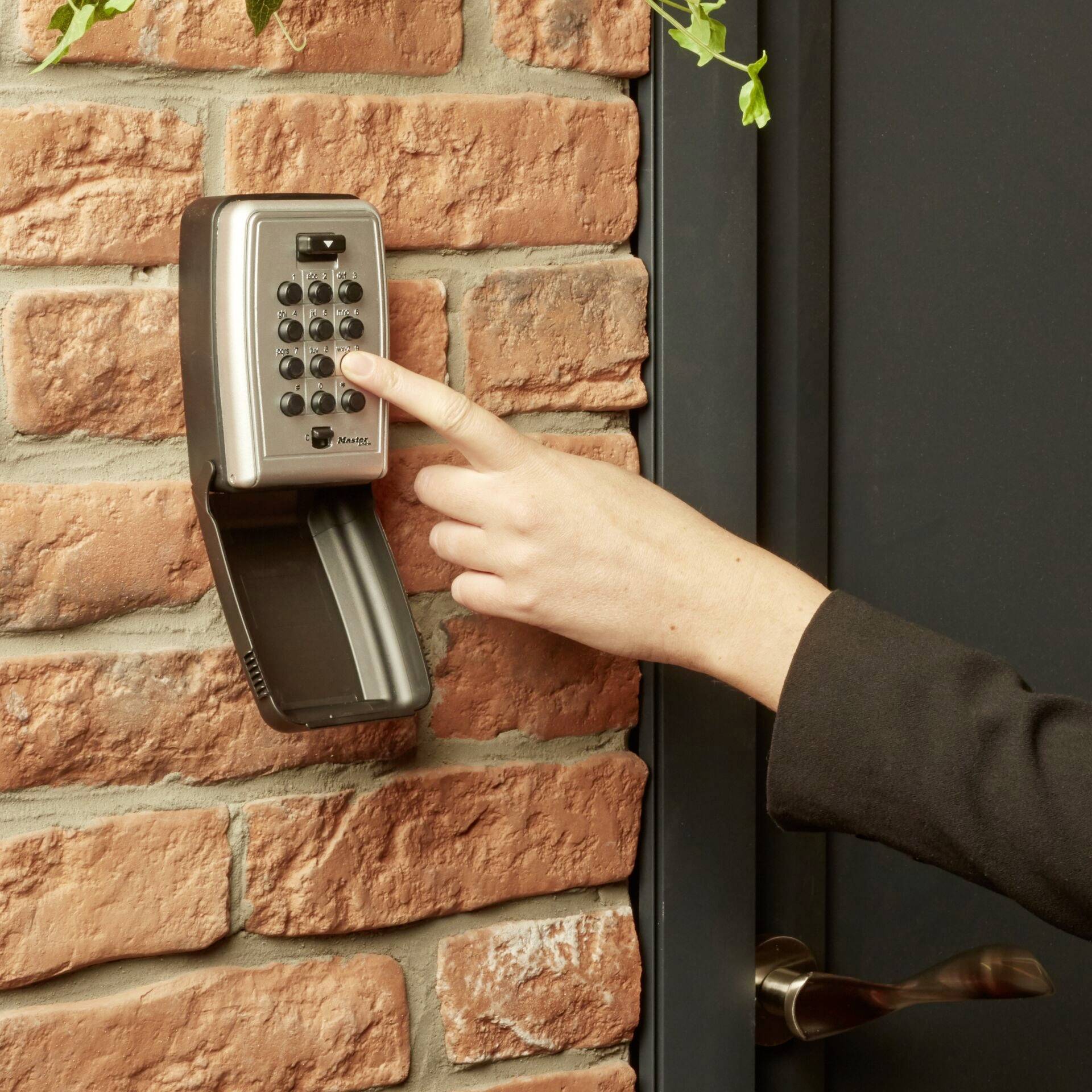 A hand pressing a button on an electronic door lock on a brick wall.